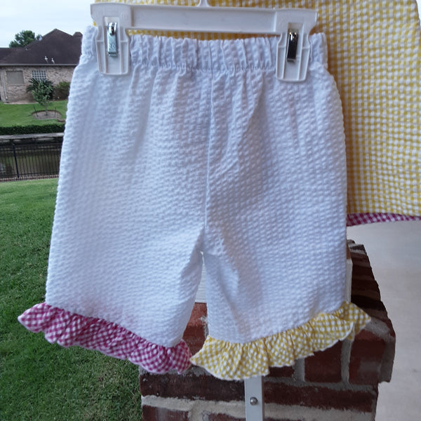 White seetsucker capris with a pink gingham ruffle on one leg and a yellow gingham ruffle on the other leg.